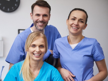 Three smiling dental team members in blue scrubs