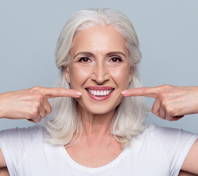 Woman pointing to healthy smile after scaling and root planing periodontal therapy